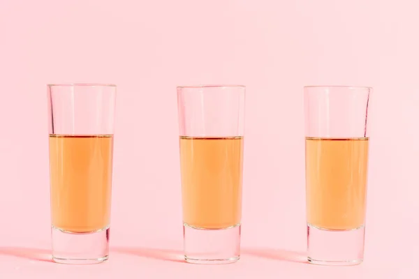 Três tiros com álcool em linha no fundo rosa — Fotografia de Stock