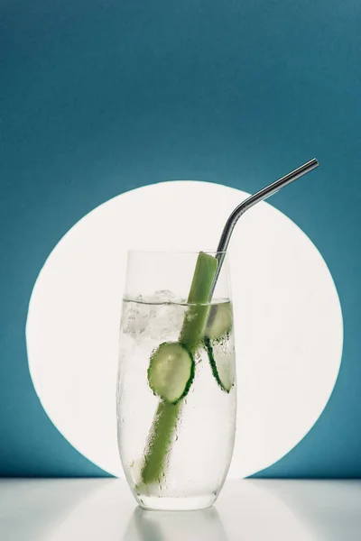 Fresh lemonade with cucumber slices, celery and straw on blue background with back light — Stock Photo