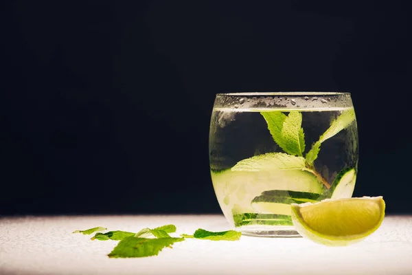 Refreshing lemonade with mint, cucumber and lime on illuminated surface isolated on black — Stock Photo