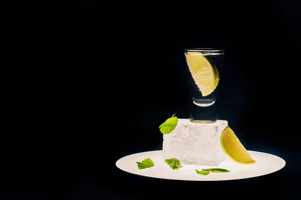 Tequila fresco con lima y menta en cubo de hielo en círculo iluminado aislado en negro - foto de stock