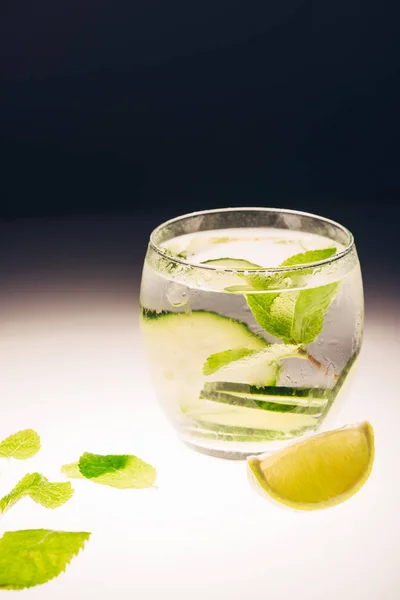 Refreshing lemonade with mint, cucumber and lime on illuminated surface on black background — Stock Photo