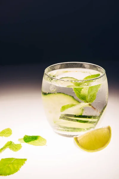 Limonata rinfrescante con menta, cetriolo e lime su superficie illuminata su fondo nero — Foto stock