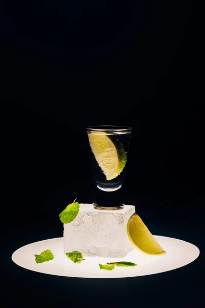 Fresh tequila with lime and mint on ice cube on illuminated circle isolated on black — Stock Photo