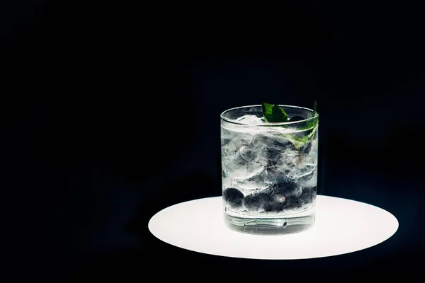 Erfrischende Limonade mit Eis und Blaubeeren auf beleuchtetem Kreis isoliert auf schwarz — Stockfoto