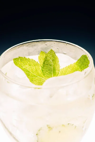 Vista de cerca de limonada refrescante fría con menta y hielo en la superficie iluminada aislada en negro - foto de stock