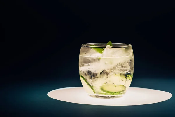 Limonata rinfrescante con menta, cetriolo e ghiaccio su cerchio illuminato isolato su nero — Foto stock