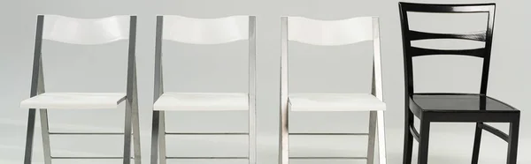 Panoramic shot of white and black chairs on grey background — Stock Photo