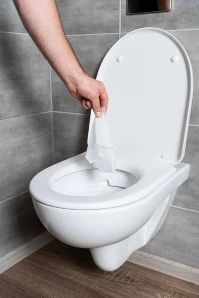 Vista recortada del hombre lanzando servilleta en el inodoro limpio en el baño - foto de stock