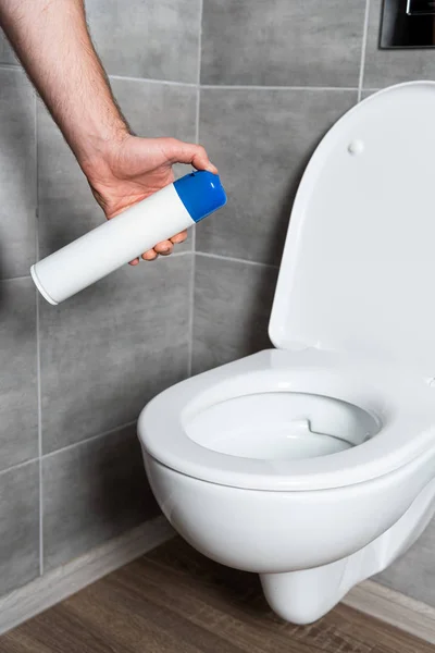 Cropped view of man holding air freshener by toilet bowl in modern bathroom — Stock Photo