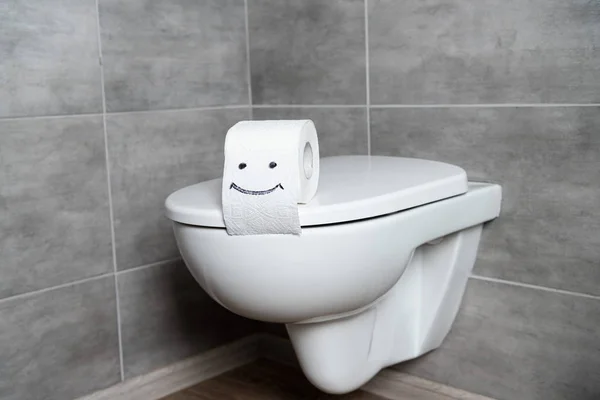 Cartel de sonrisa sobre papel higiénico en asiento de inodoro blanco en baño con baldosas grises - foto de stock
