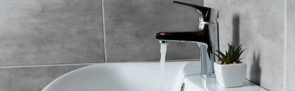 Panoramic shot of flowing water from sink to washbasin with plant in restroom — Stock Photo