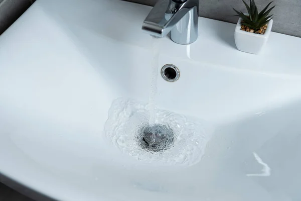 Vue à angle élevé de l'eau qui coule de l'évier au lavabo propre avec plante dans la salle de bain — Photo de stock