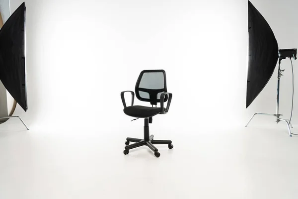 Schwarzer Bürostuhl mit Studioleuchte auf weißem Hintergrund — Stockfoto