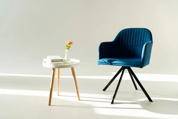 Blauer moderner Sessel und Couchtisch mit Blume in Vase und Büchern auf grauem Hintergrund — Stockfoto