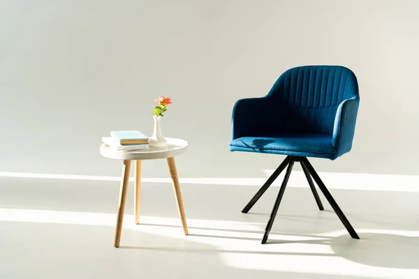 Fauteuil moderne bleu et table basse avec fleur dans un vase et livres sur fond gris — Photo de stock