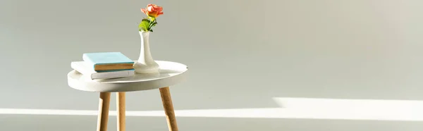 Panoramic shot of coffee table with rose in vase and books on grey background — Stock Photo