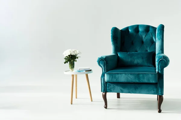 Sillón turquesa por mesa de centro con flores y libros sobre fondo gris - foto de stock