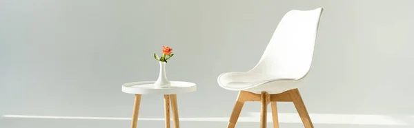 Panoramic shot of modern chair by table with rose in vase on grey background — Stock Photo