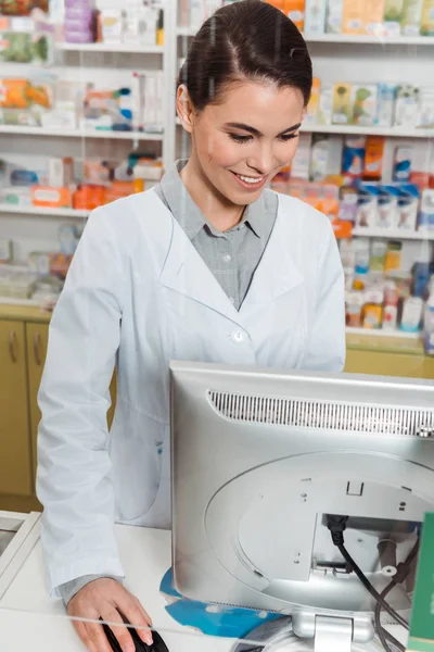 Farmacêutico sorridente atraente usando computador na farmácia — Fotografia de Stock