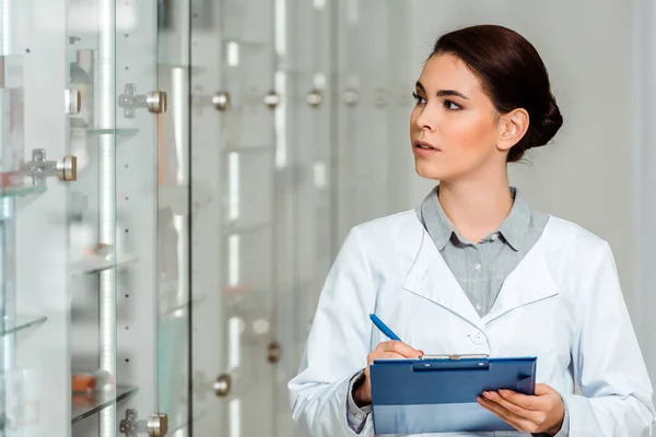 Pharmacist with clipboard looking at showcase in drugstore — Stock Photo