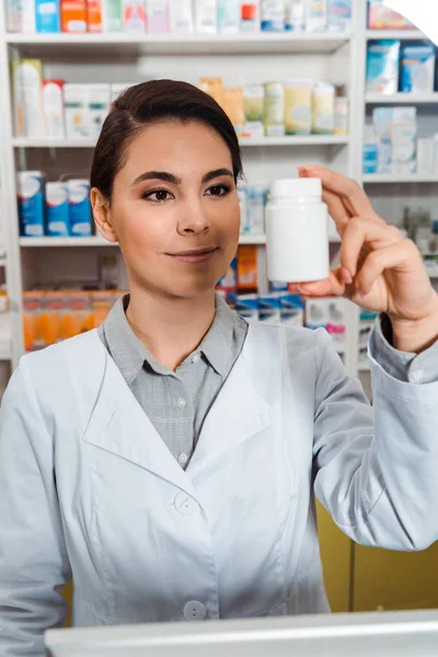 Привлекательный фармацевт держит банку с таблетками в аптеке — стоковое фото