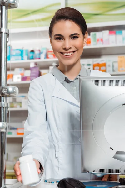 Красивий фармацевт посміхається на камеру, тримаючи таблетки за лічильником — стокове фото