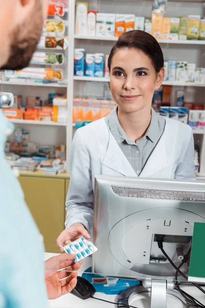Selective focus of smiling druggist giving pills to customer at pharmacy counter — Stock Photo