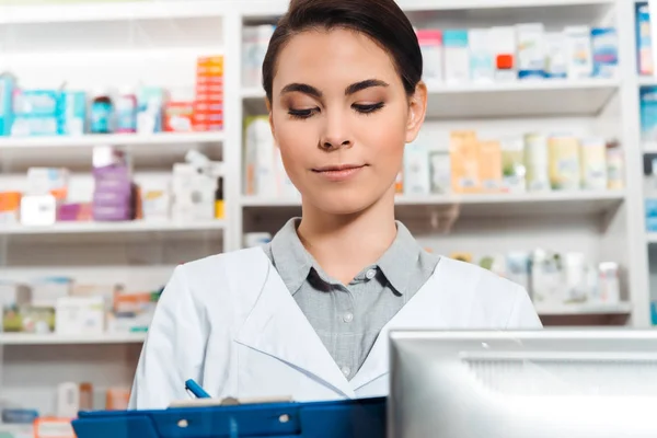 Hermoso farmacéutico escribiendo en portapapeles en la farmacia - foto de stock