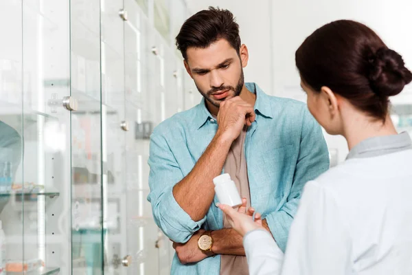 Selective focus of througful customer and pharmacist with pills in apothecary — Stock Photo