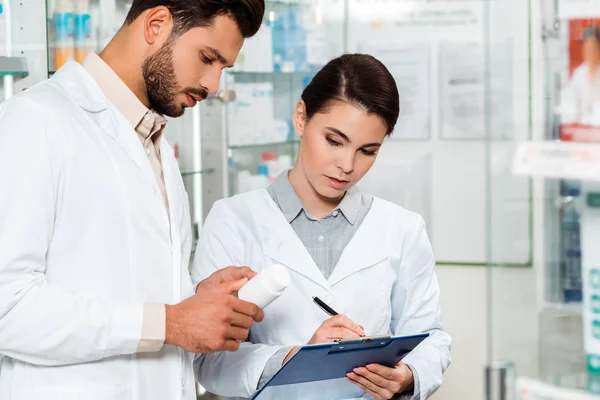 Farmacéutico con pastillas y portapapeles en farmacia - foto de stock