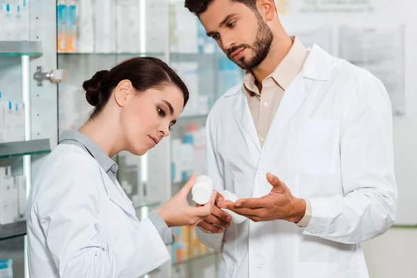 Pharmacists in white coats looking at jar with pills in pharmacy — Stock Photo