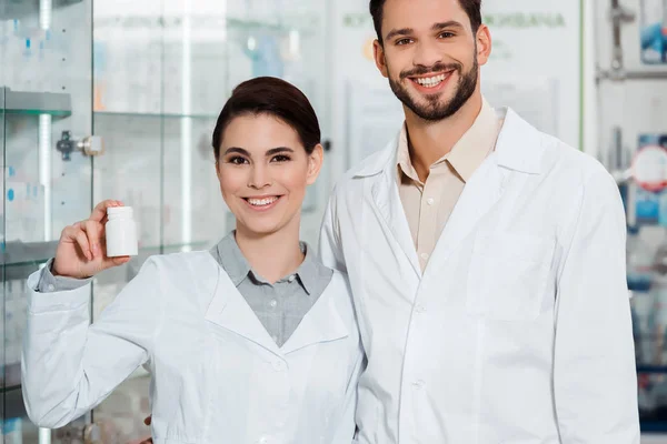 Farmacisti sorridenti con pillole che guardano la macchina fotografica in farmacia — Foto stock