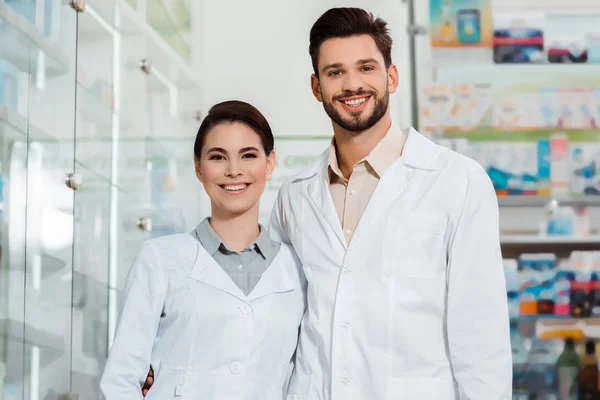 Pharmaciens en blouse blanche souriant à la caméra en pharmacie — Photo de stock