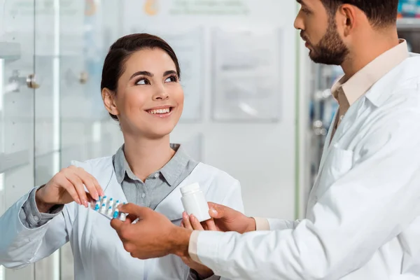 Pharmacist giving pills to smiling colleague in drugstore — Stock Photo