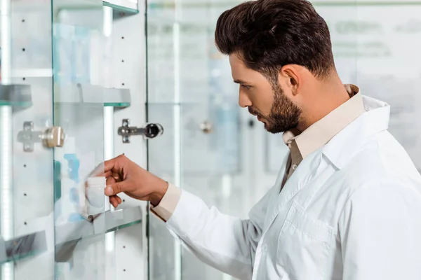 Seitenansicht eines Apothekers, der Pillen aus dem Vitrinenregal nimmt — Stockfoto