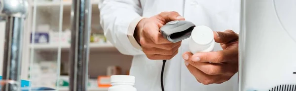 Обрезанный вид аптекаря со сканером штрих-кода и таблетками на прилавке аптеки, панорамный снимок — стоковое фото