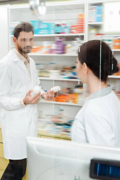 Enfoque selectivo del farmacéutico con pastillas mirando al colega en el mostrador de la farmacia - foto de stock