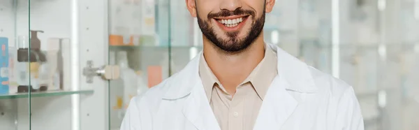 Vista cortada do farmacêutico sorrindo para a câmera em boticário, tiro panorâmico — Fotografia de Stock