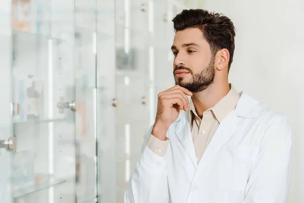 Droguiste pensif regardant les étagères vitrine en pharmacie — Photo de stock
