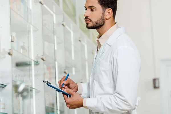 Vista laterale del bel farmacista con appunti guardando vetrina farmacia — Foto stock