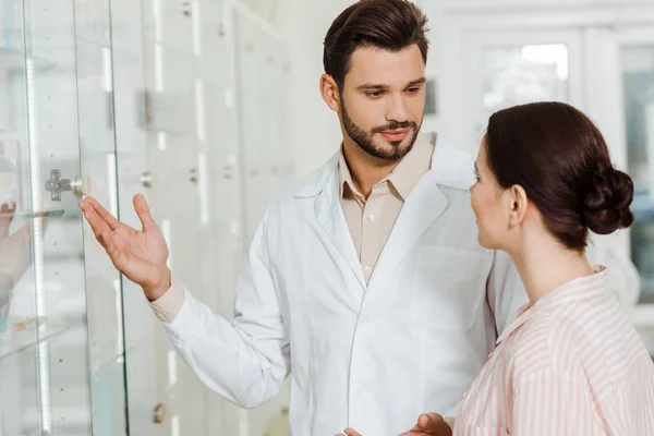 Pharmacist pointing at drugstore showcase to customer — Stock Photo