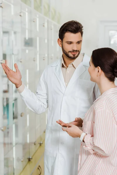 Beau pharmacien pointant vers la vitrine au client en pharmacie — Photo de stock