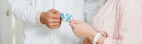 Cropped view of druggist giving blister with pills to female customer, panoramic shot — Stock Photo