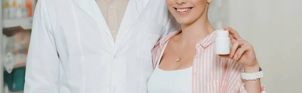 Vista ritagliata del cliente sorridente che mostra vaso di pillole accanto al farmacista, colpo panoramico — Foto stock