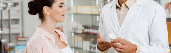 Vista laterale del farmacista mostrando al vaso cliente femminile di pillole, colpo panoramico — Foto stock