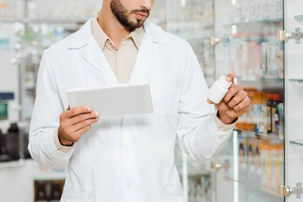Обрезанный вид аптекаря с цифровым планшетом и баночкой с таблетками от аптекарской витрины — стоковое фото