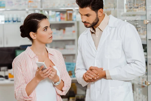 Customer showing to pharmacist smartphone by drugstore showcase — Stock Photo
