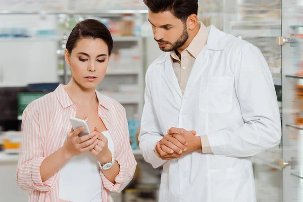 Femme client montrant au smartphone pharmacien par vitrine de la pharmacie — Photo de stock