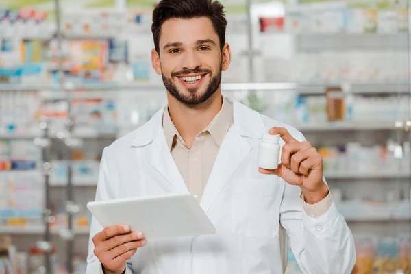Apotheker lächelt in die Kamera, während er Tabletten und Tabletten in der Apotheke hält — Stockfoto