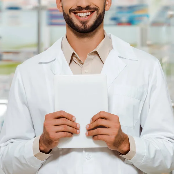 Обрезанный вид улыбающегося фармацевта в белом халате с цифровым планшетом — стоковое фото